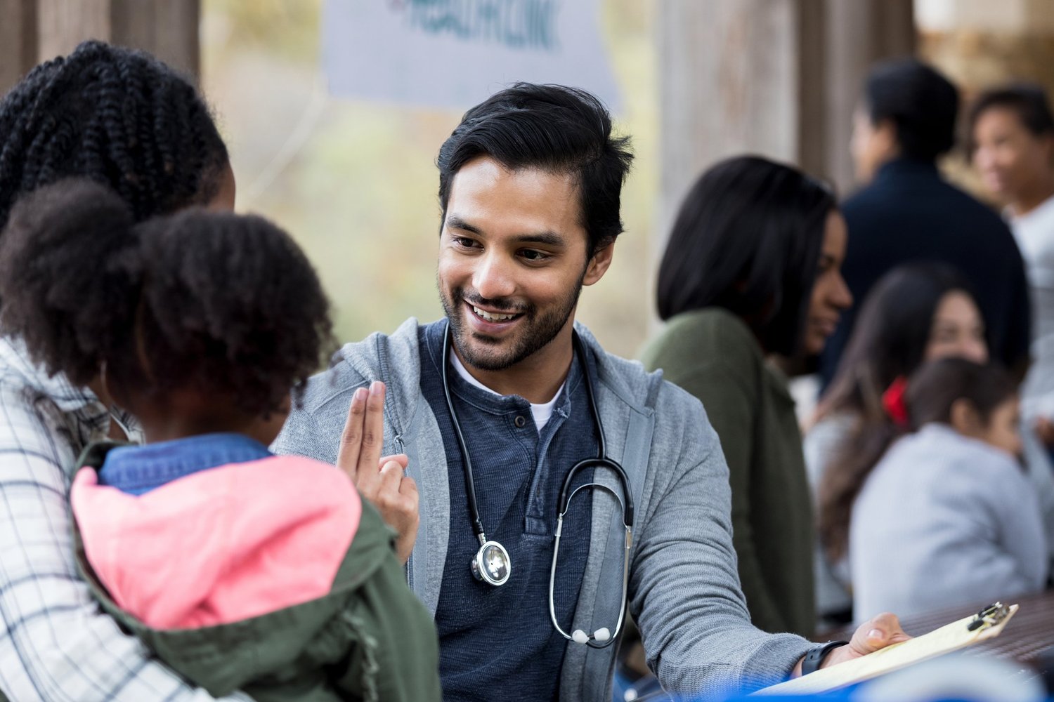 Volunteer doctor holds up two fingers as he checks a young girl's vision. The girl and her mom are visiting an outdoor free clinic.